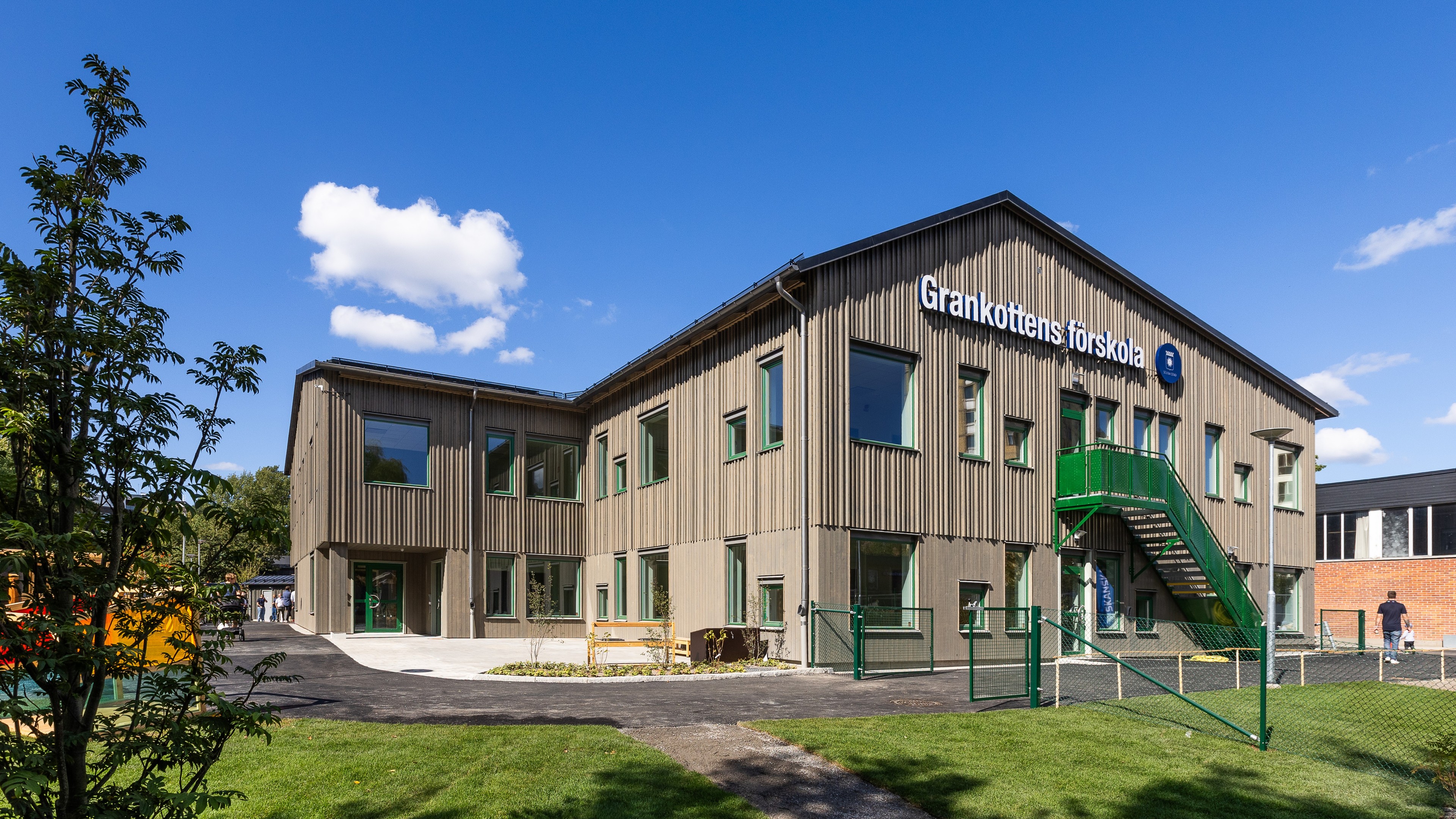 Modern träförskolebyggnad med namnet Grankottens förskola under en klarblå himmel.