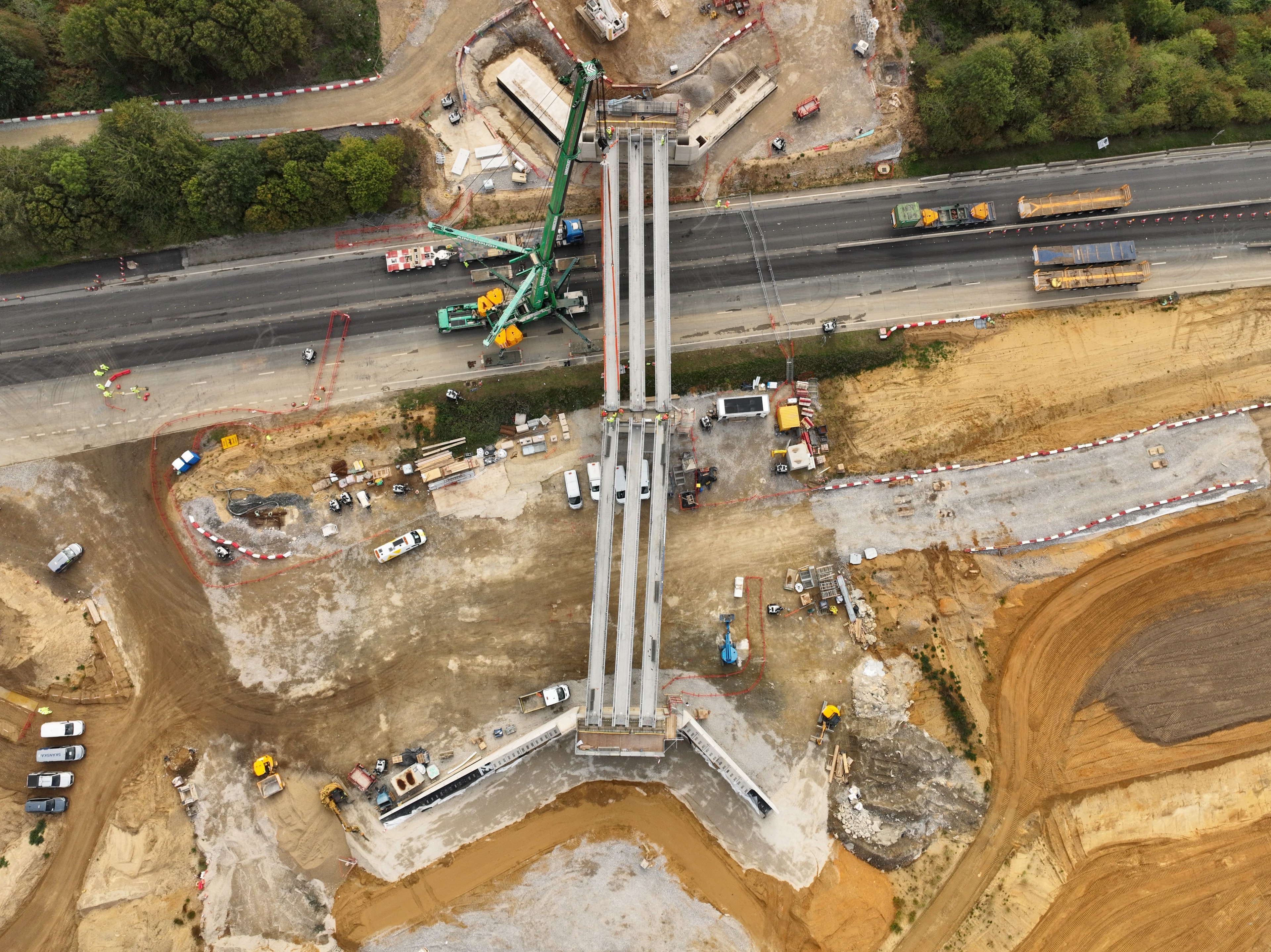 Six beams installed across the A11 in Norfolk for a new bridge on the A47 project. Aerial view of a highway bridge under construction with cranes and construction vehicles.