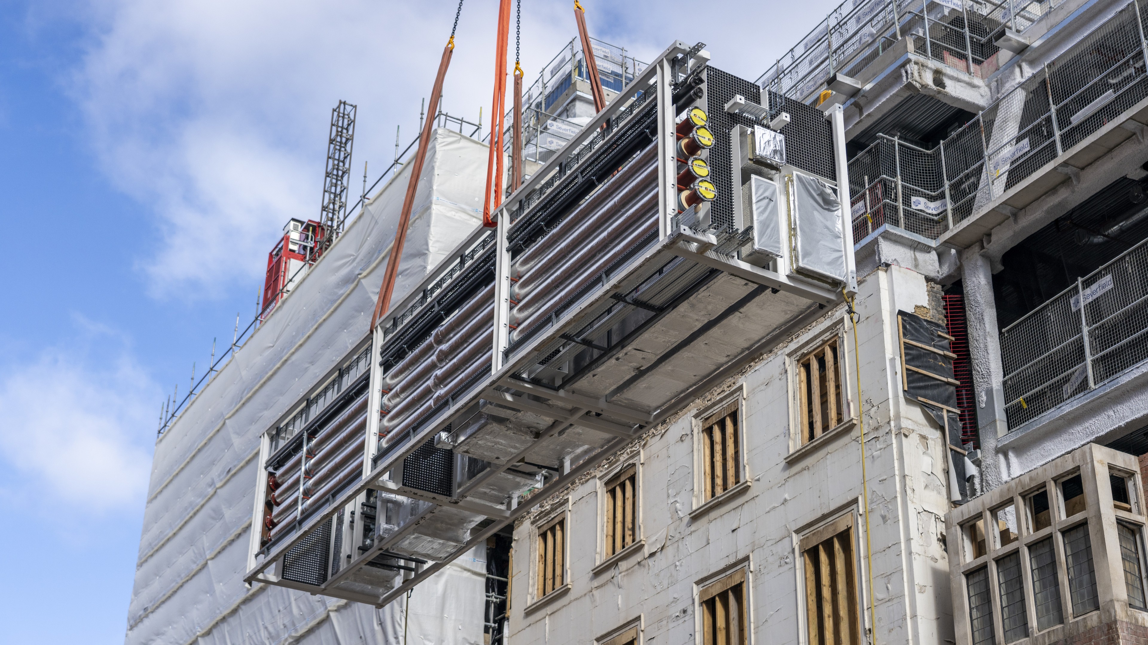 Industrial HVAC unit being installed on site Large industrial HVAC unit being lifted by crane at a construction site with scaffolding.