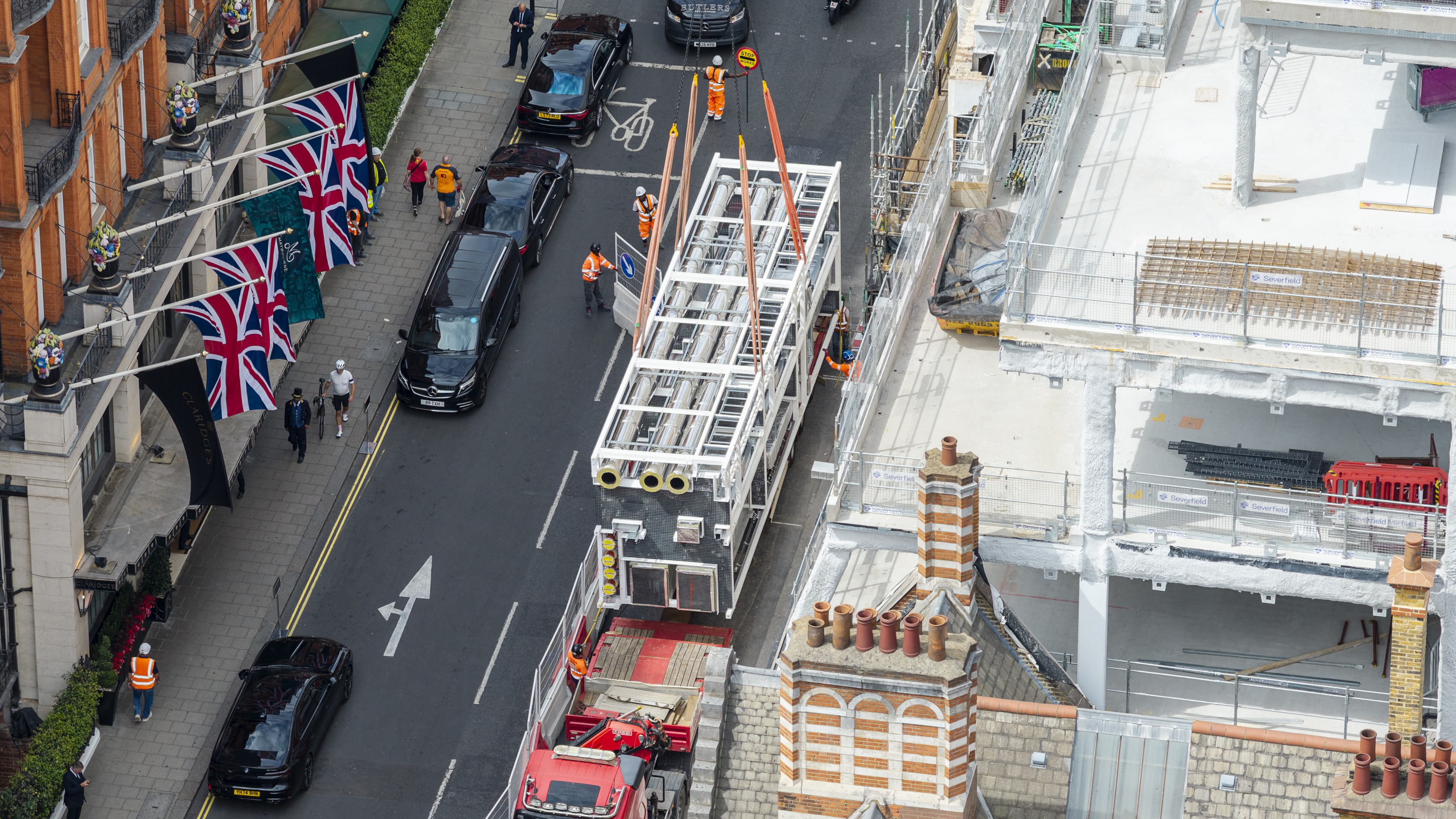 Aerial view of a London street with Union Jack flags and vehicles including a crane.