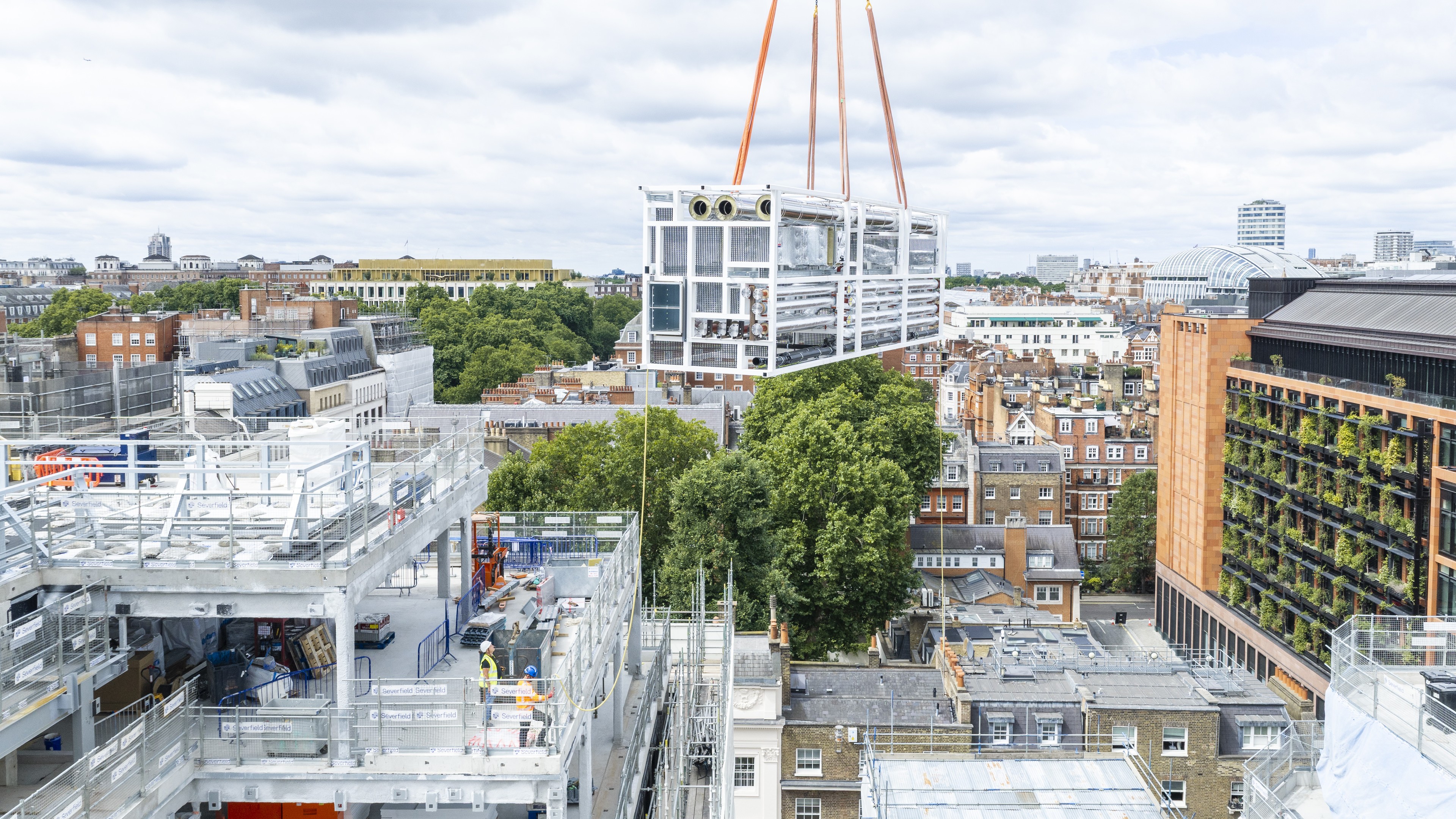 Modular building unit lifted by crane over urban construction site with cityscape background.