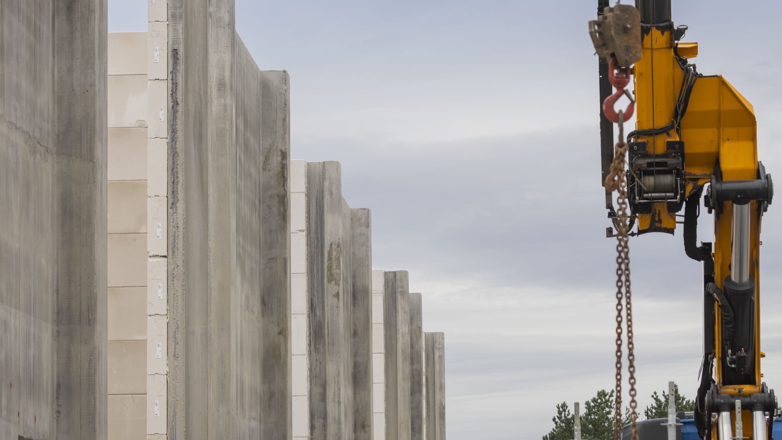 Construction site with large concrete walls and a yellow crane under a cloudy sky.