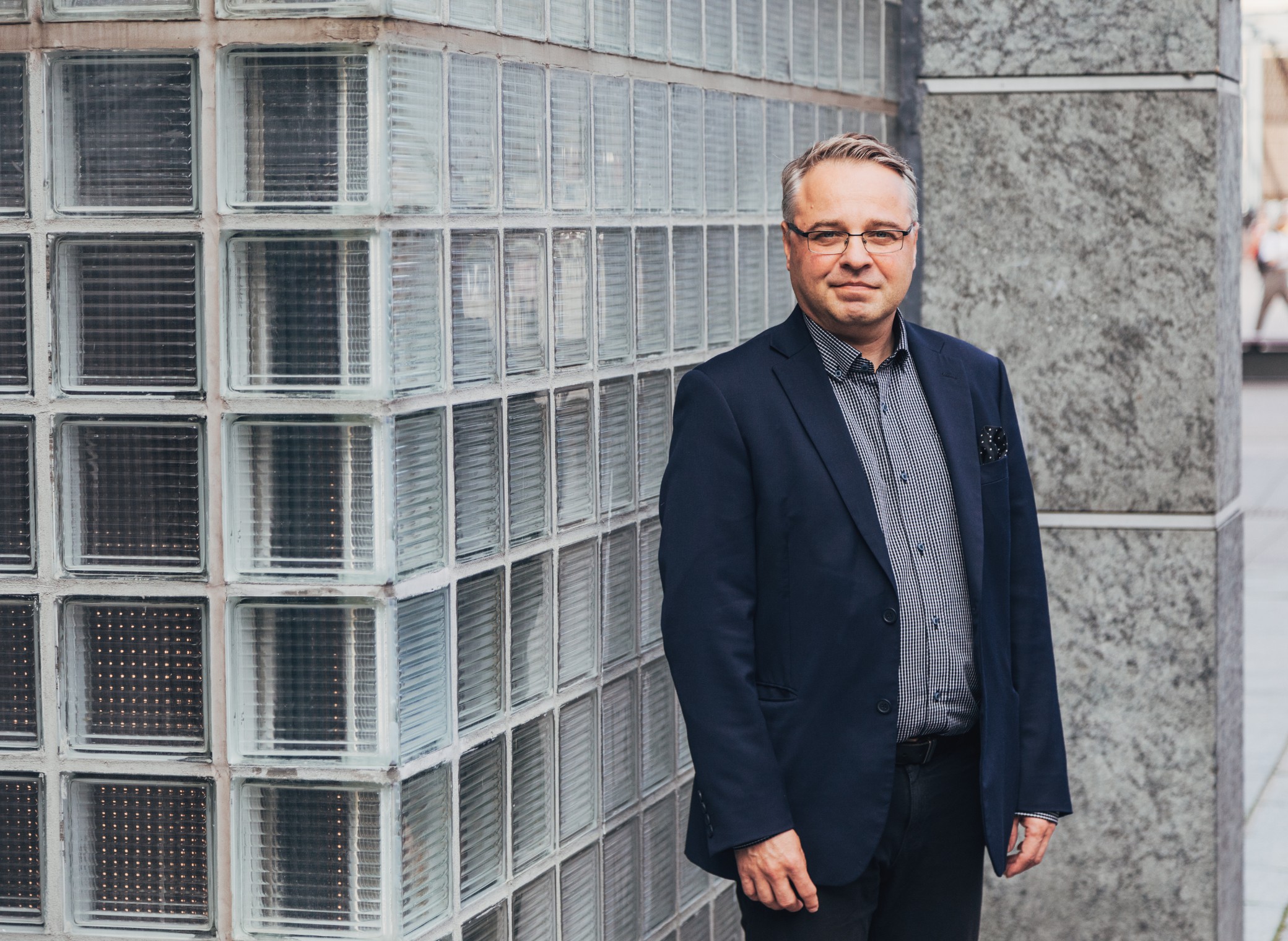 Mies seisoo ulkona rakennuksen seinän edessä ja katsoo kameraan