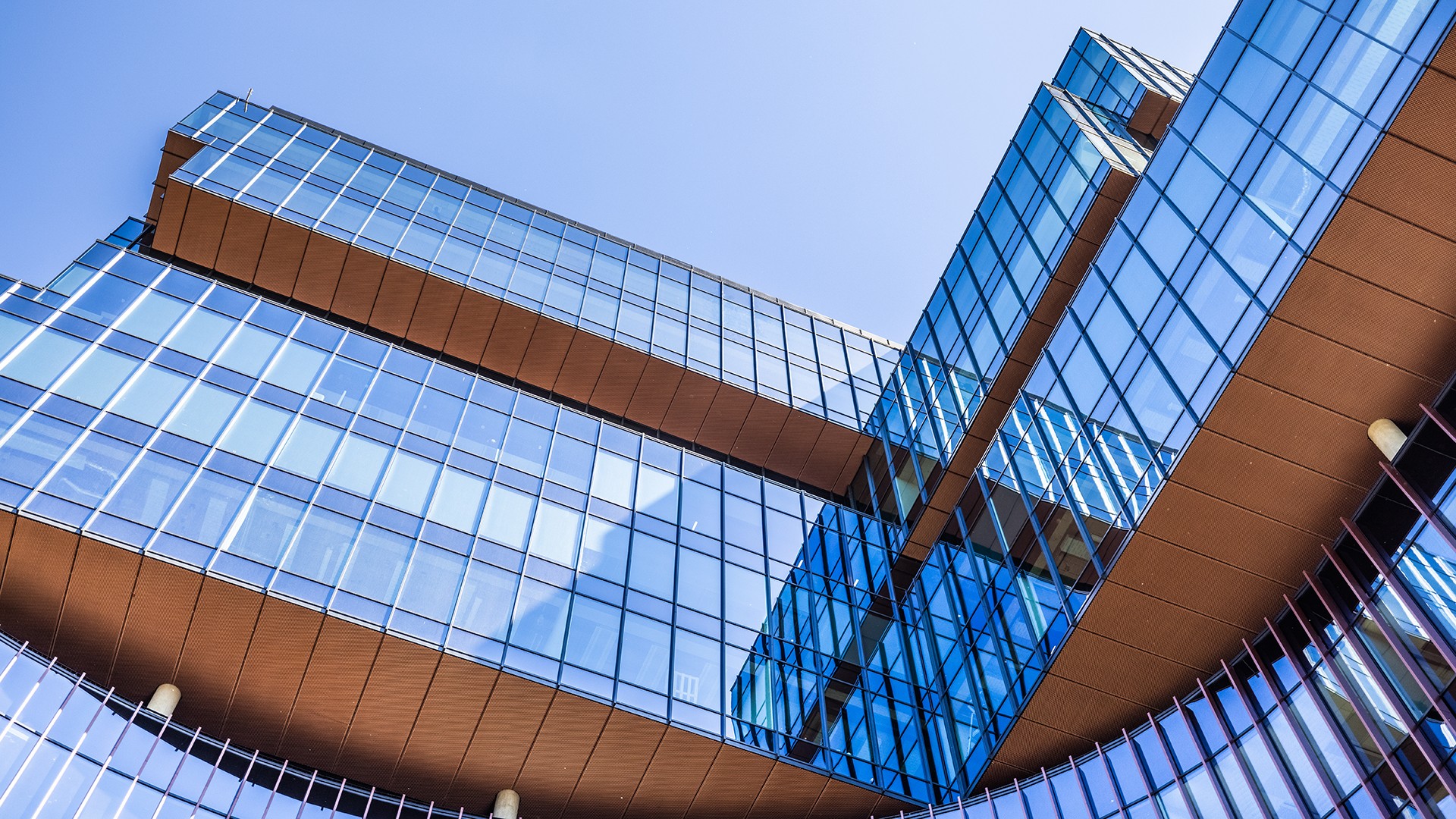 Modern glass building with angular design and sky reflection under clear blue skies.