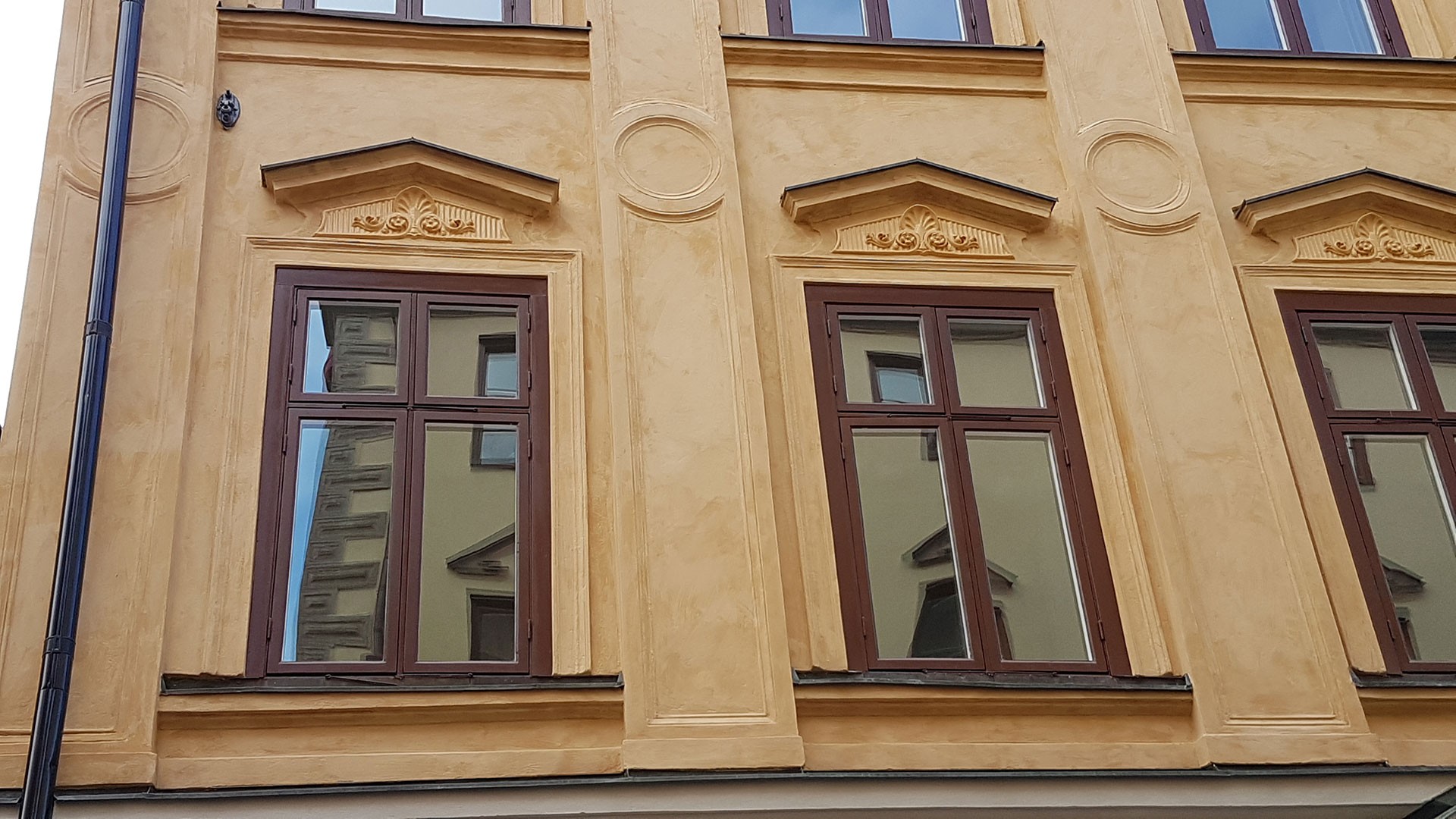 Gul byggnadsfasad med dekorativa fönsterramar som reflekterar en annan byggnads bild.