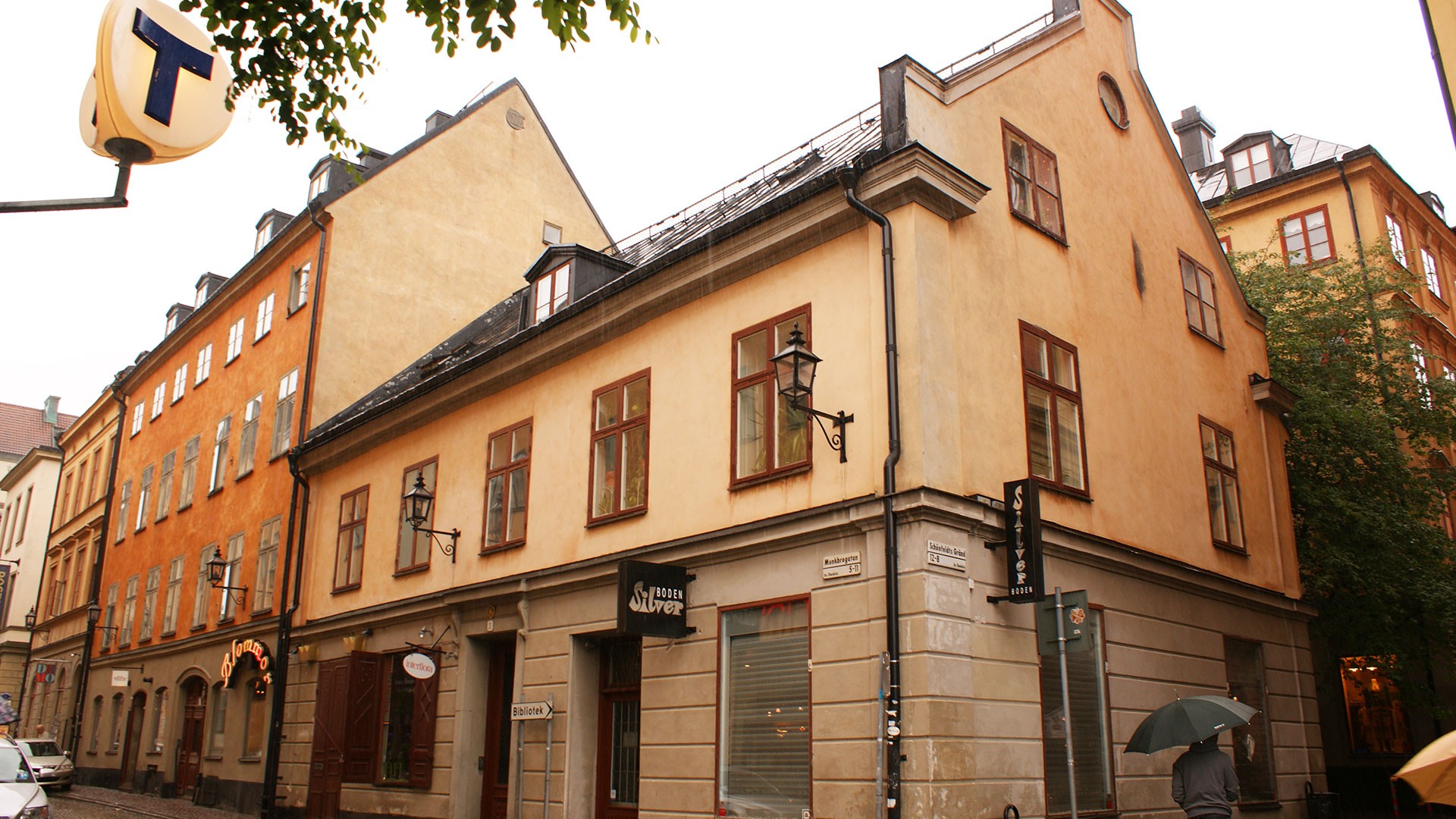 Historisk svensk arkitektur med ockrafärgade väggar och träfönster under en regnig himmel.