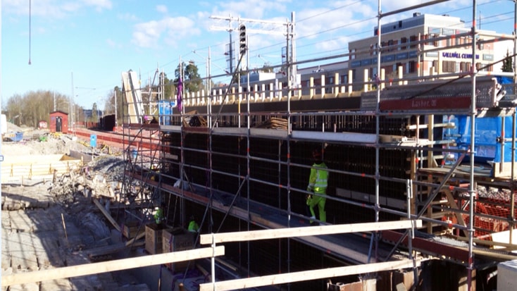 Det nya stationshuset stod färdigt under sensommaren 2016. Byggnadsarbetare bygger en betongkonstruktion med byggnadsställningar på en livlig stadsplats.