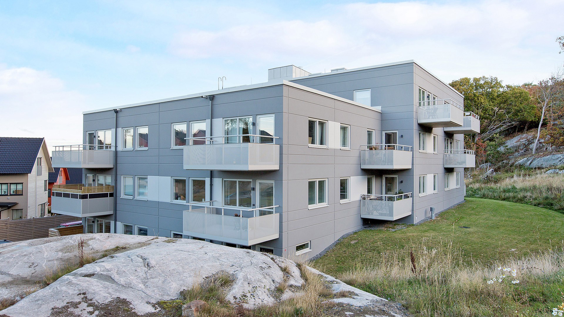 Modernt flerbostadshus med balkonger, beläget på ett stenigt landskap.