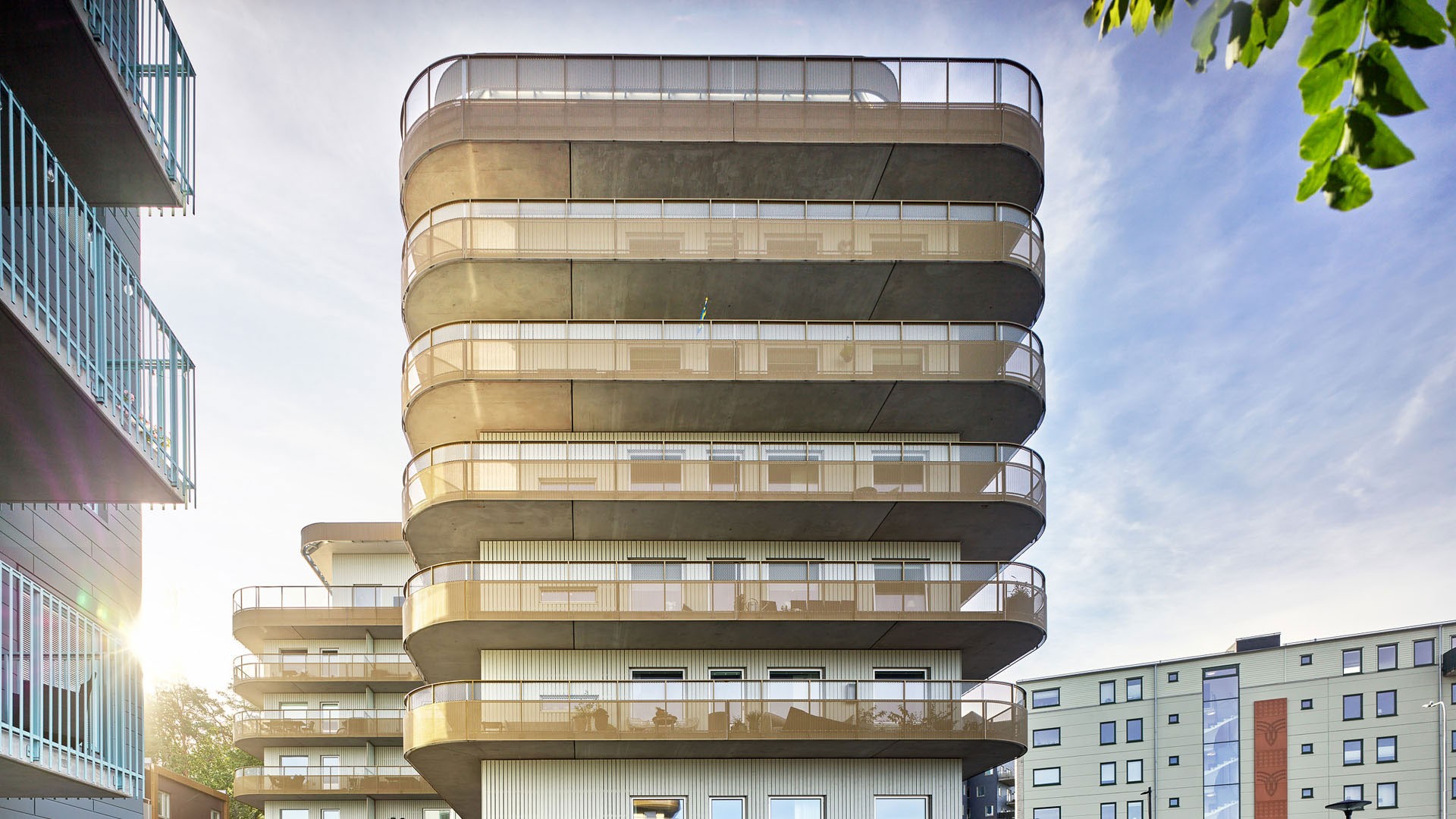 Modern byggnad med flera våningar och böjda balkonger samt en elegant design, fotograferad vid solnedgång.