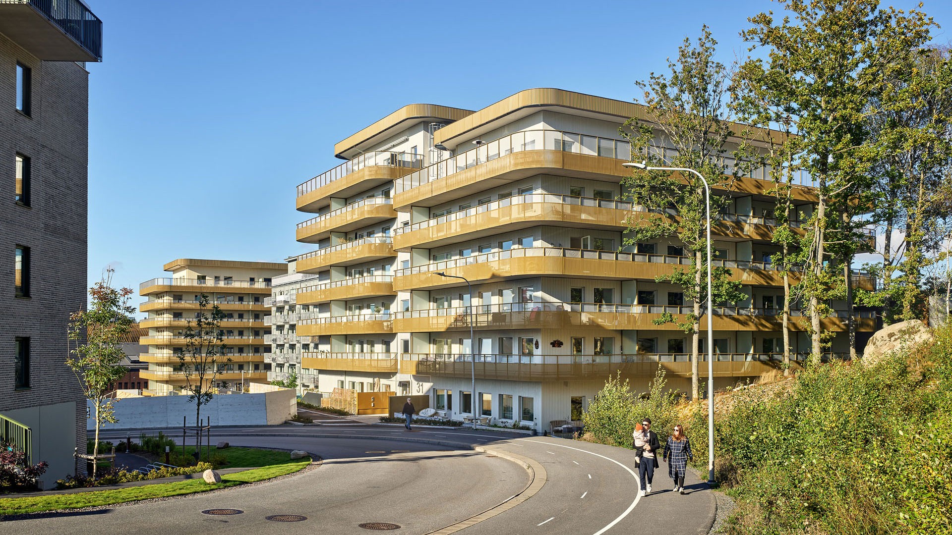 Moderna lägenhetsbyggnader med runda balkonger omgivna av grönska på en solig dag.