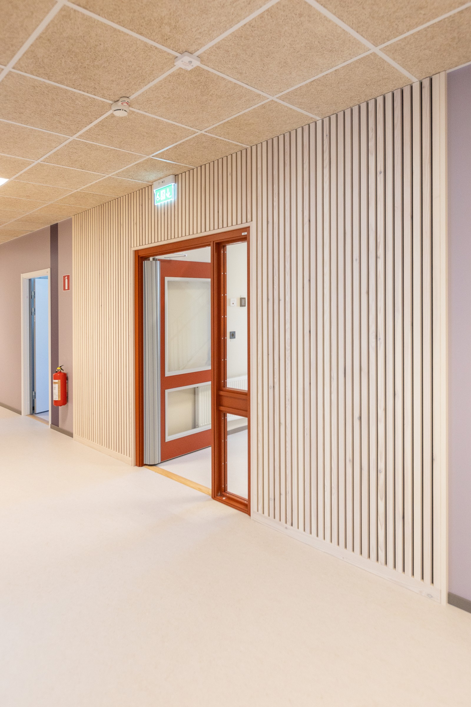 Korridor i Västerängsskolan med väggpanel i trä och dörrar i rödbrunt trä, som skapar en varm och trivsam miljö.