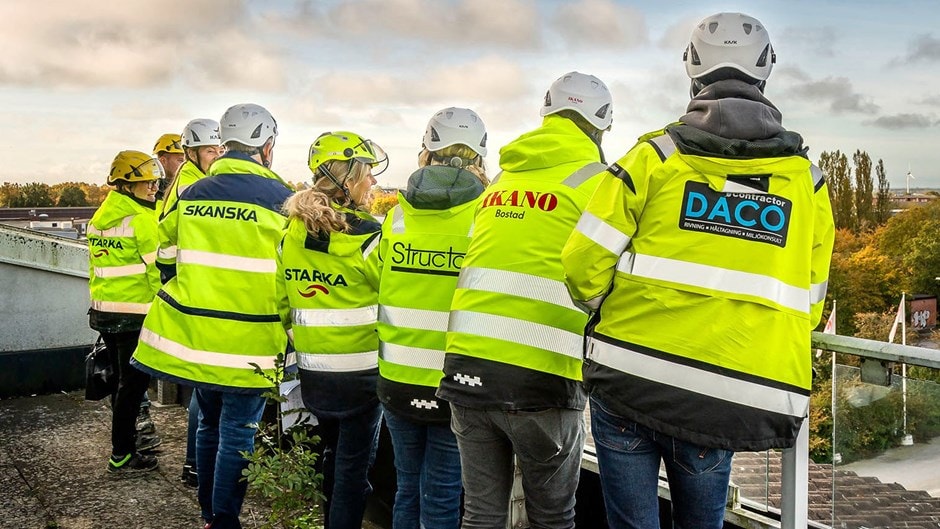 Samarbete är nyckeln till framgång. Grupp av byggnadsarbetare som bär säkerhetsutrustning och varseljackor på arbetsplatsen.