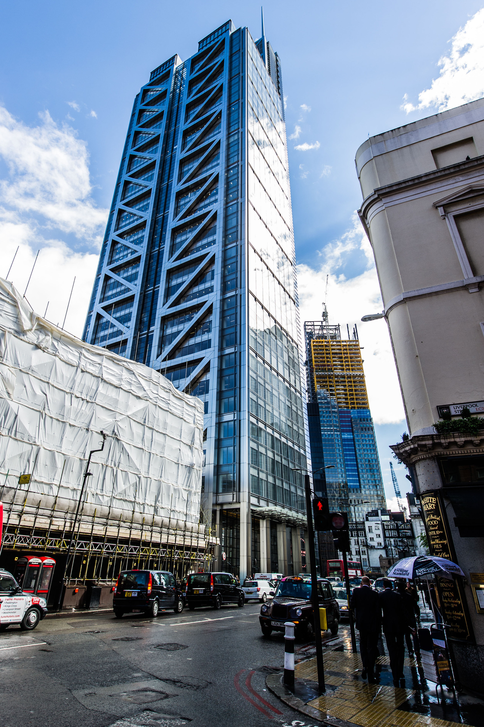Heron Tower Modern skyscraper with glass facade on a busy London street, surrounded by construction work.