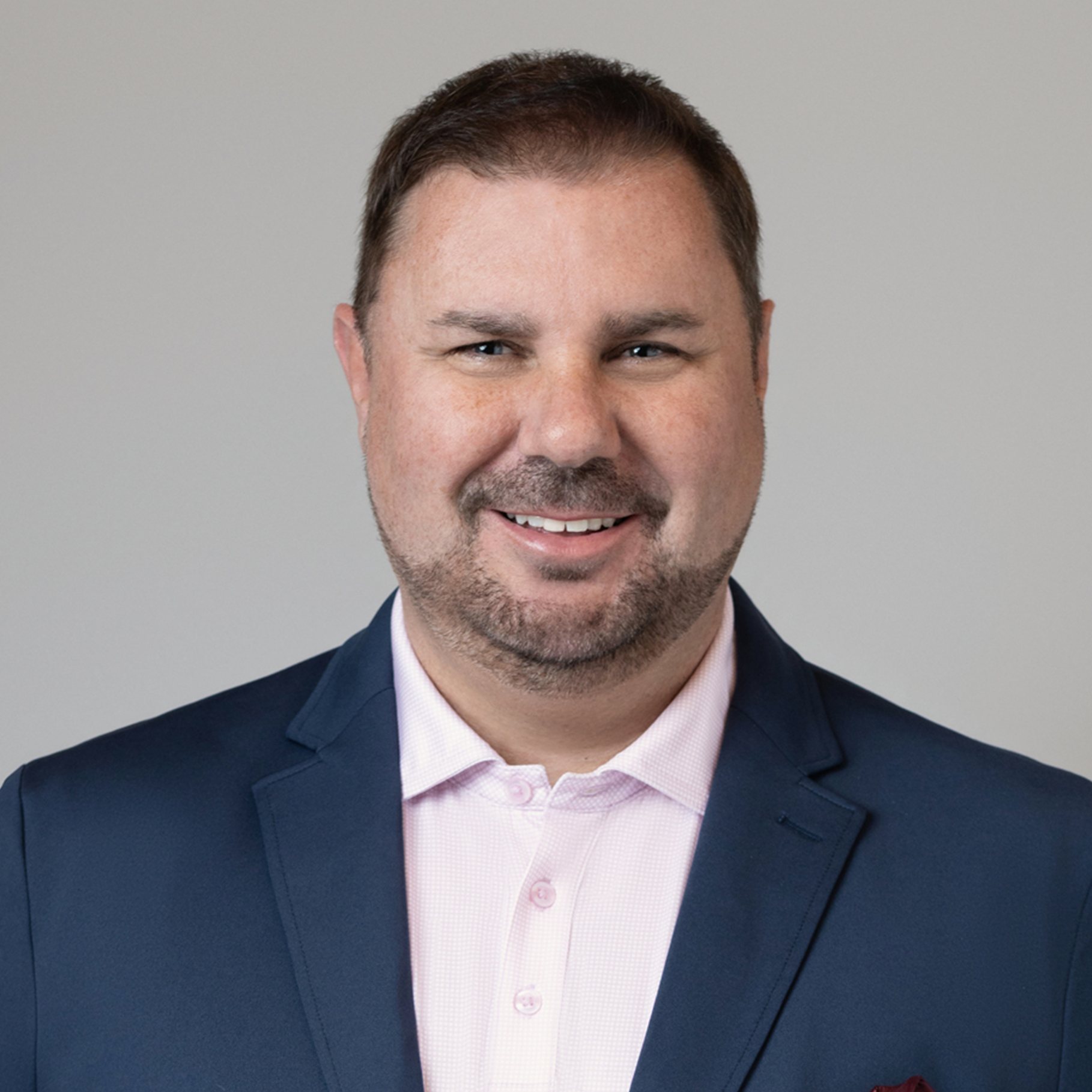 Stephen wearing a navy blazer and light pink button-up shirt against a plain background.