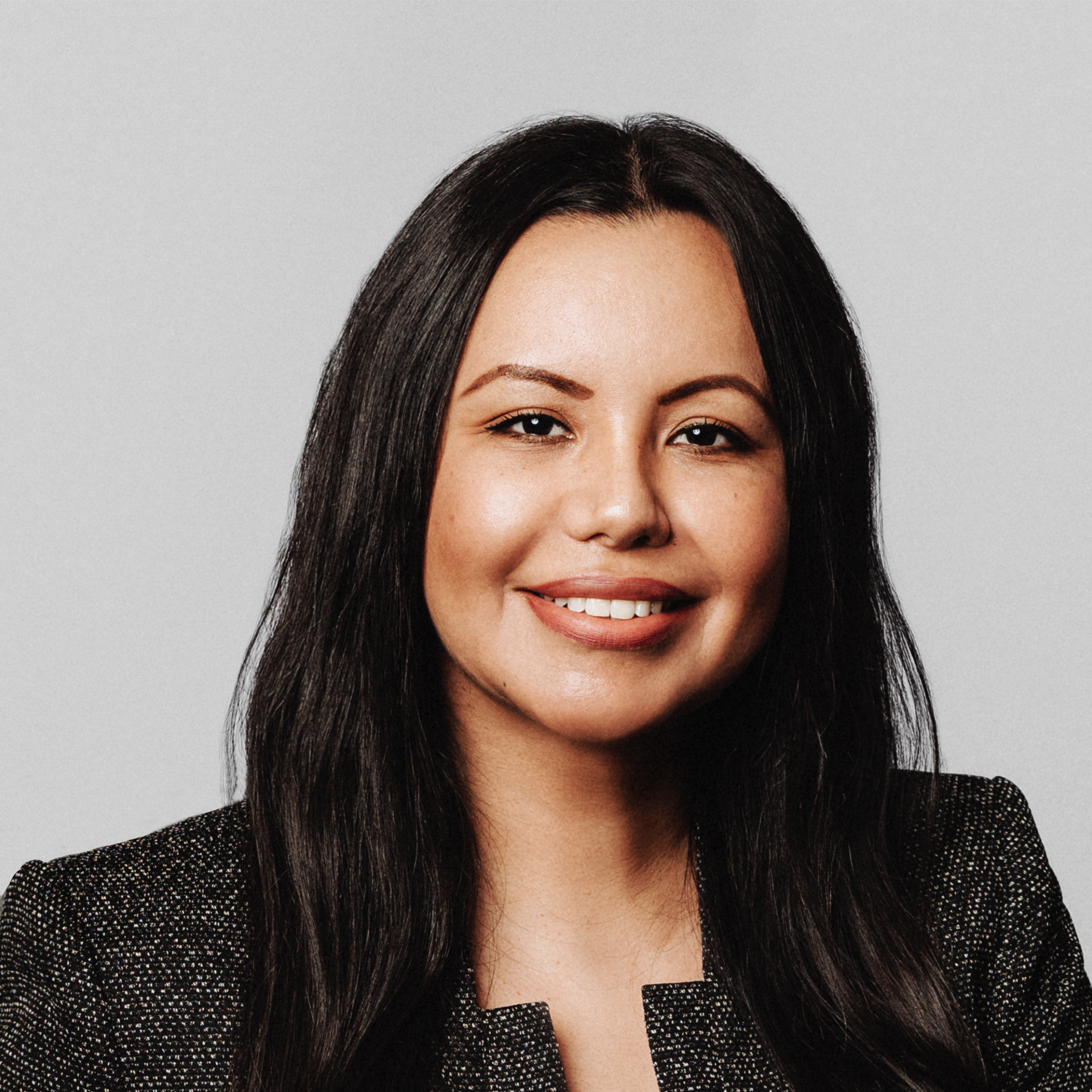 Professional woman with long dark hair in business attire Professional woman with long black hair wearing a dark textured blazer on gray background.