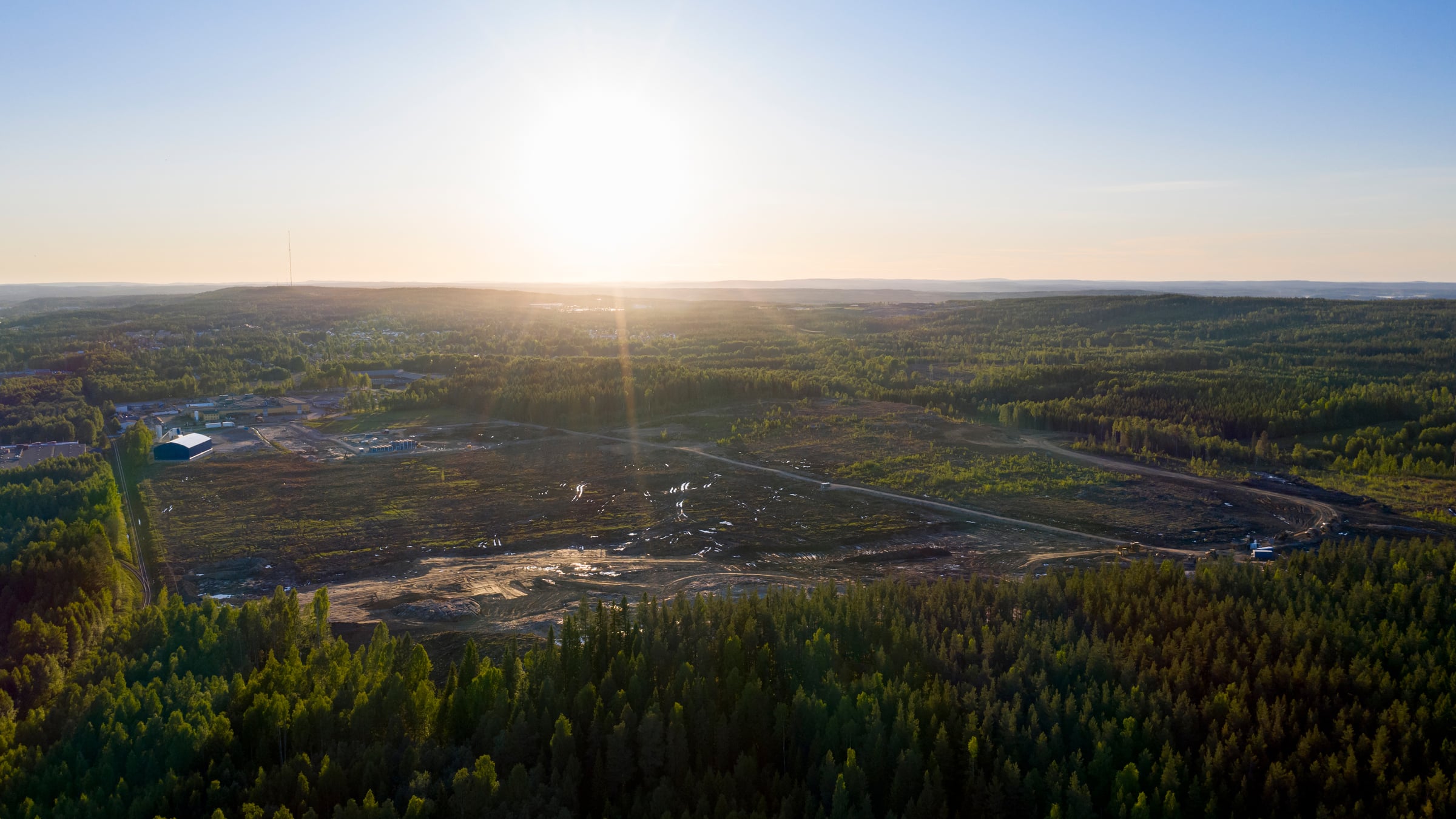 Skellefteå Site East covers 45 hectares and is located in Hedensbyn just a few kilometers outside Skellefteå's city center. Aerial view of a forested landscape at sunrise with cleared land and scattered development.