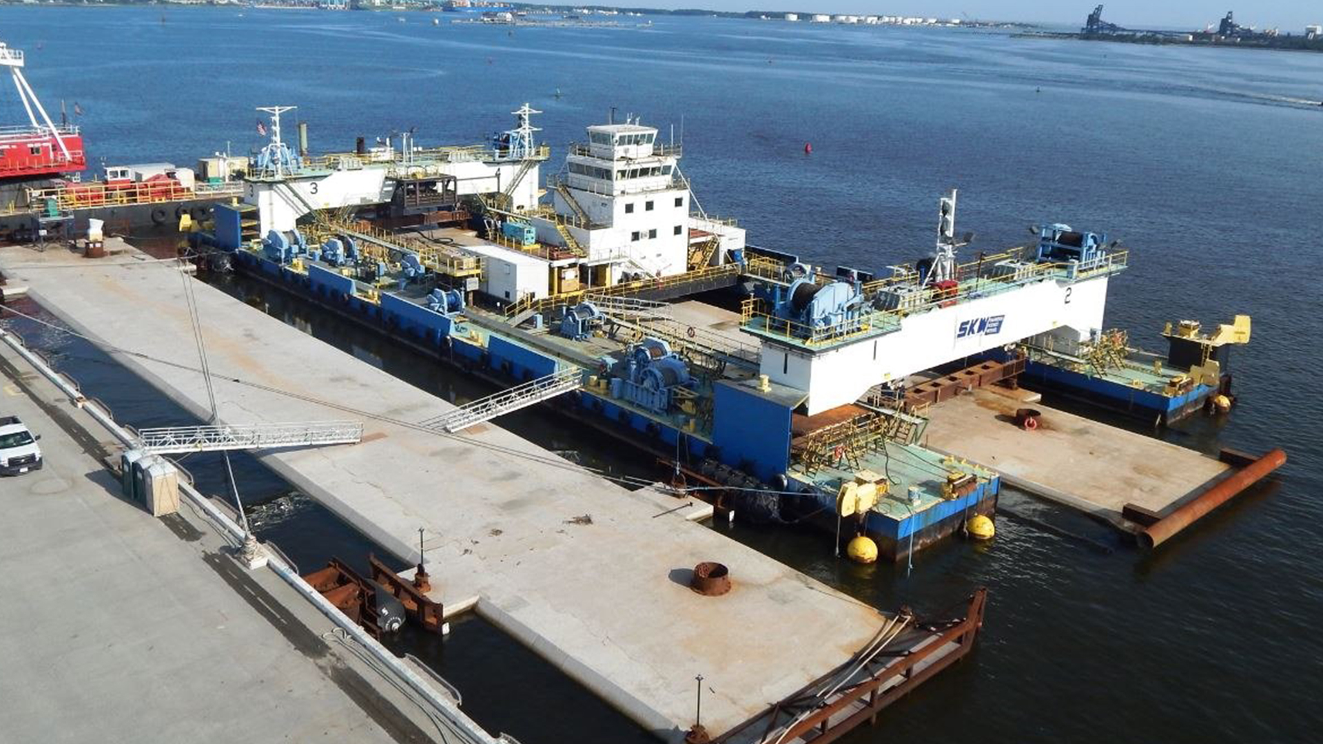 Large industrial ship docked at a harbor with clear blue water and surrounding pier.