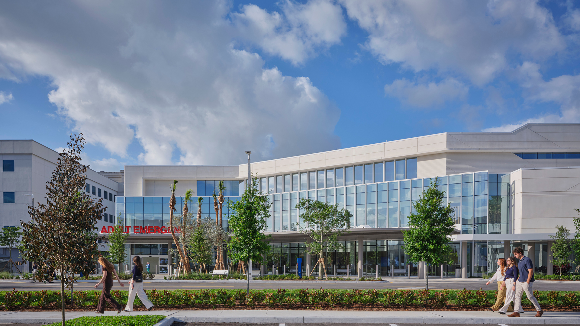 Modern Hospital Exterior with People Walking Outside on Sunny Day Modern hospital building with emergency entrance and people walking outside on a sunny day.