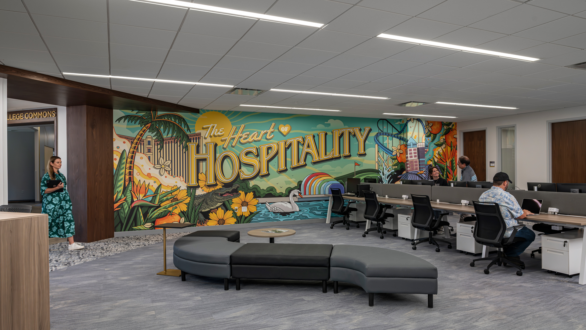 Modern office space with curved seating, desks, and a colorful "Hospitality" mural.