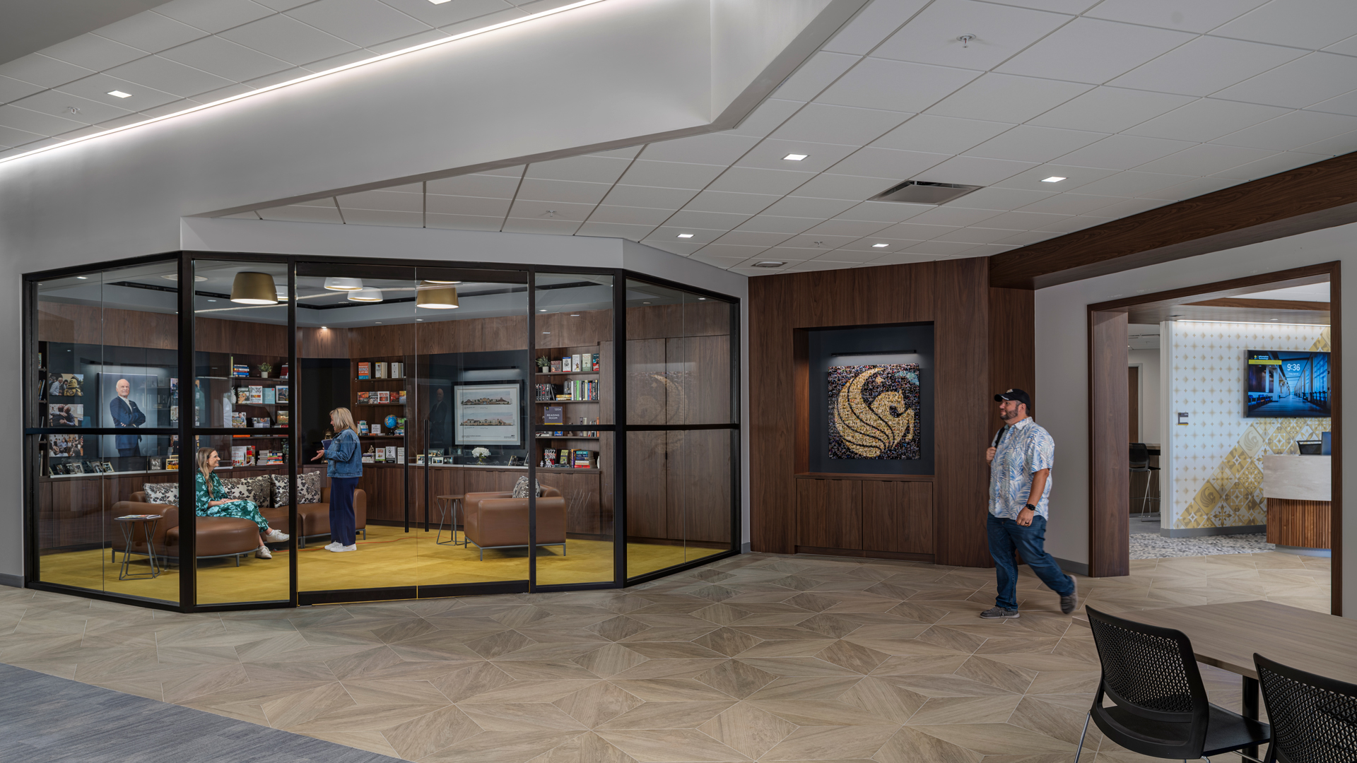 Modern office lounge with glass walls, people conversing, and stylish interior design.