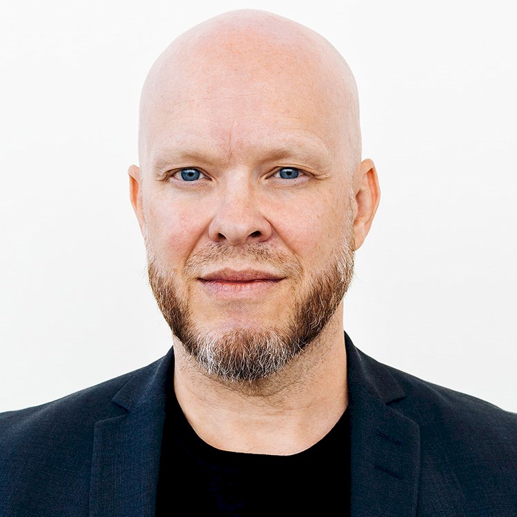 Bald man wearing a black shirt and blazer against a white background.