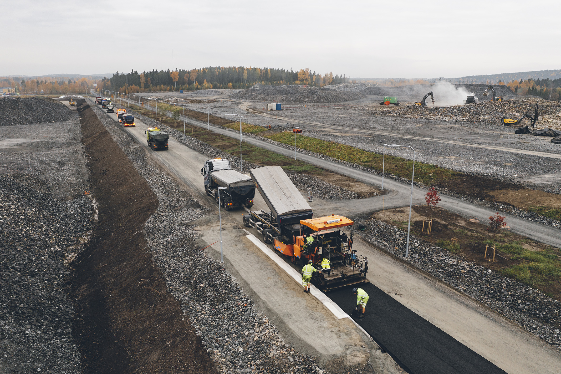 Parallellt med projekteringen i Fas 1 togs även ett hållbarhetsprogram fram med fokus på tre hållbarhetsaspekter; ekonomisk, ekologisk och social. Vägarbetsplats med maskiner och arbetare som lägger asfalt, omgiven av stenig terräng.